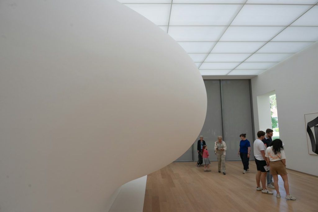 Çağdaş sanat sergisi atmosferini temsil eden beyaz soyut heykelin bulunduğu galeri görünümü